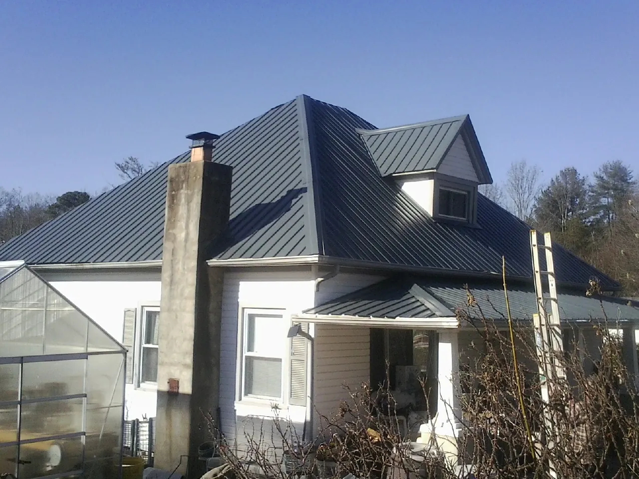 Dark blue standing seam metal roof on a white farmhouse with dormer — Slate & Tile Roof Repair by Roofing Brothers in Weldona