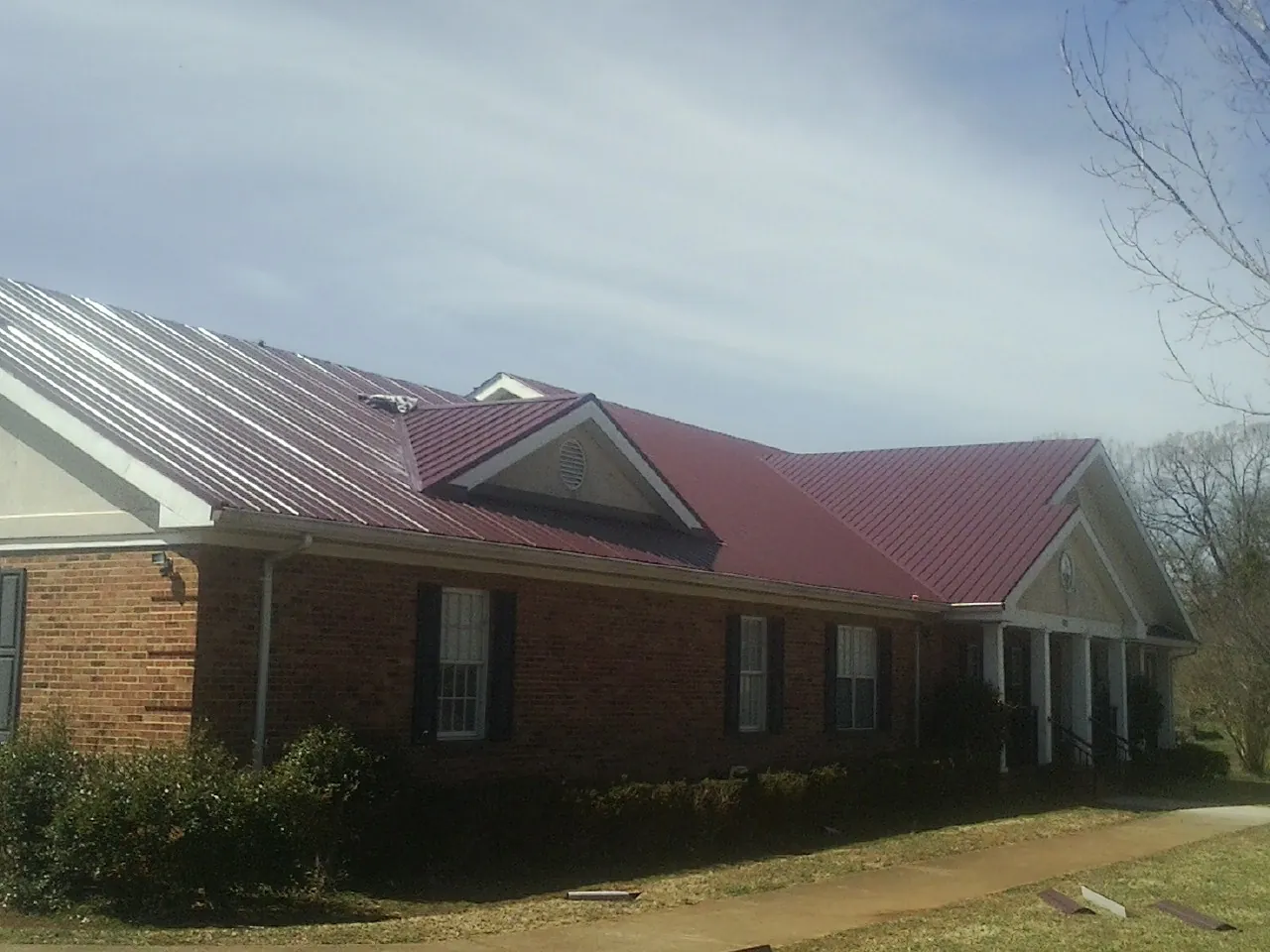 Red metal roof with gabled entries on a long brick building, from a Hail Damage Roof Repair job in Weldona