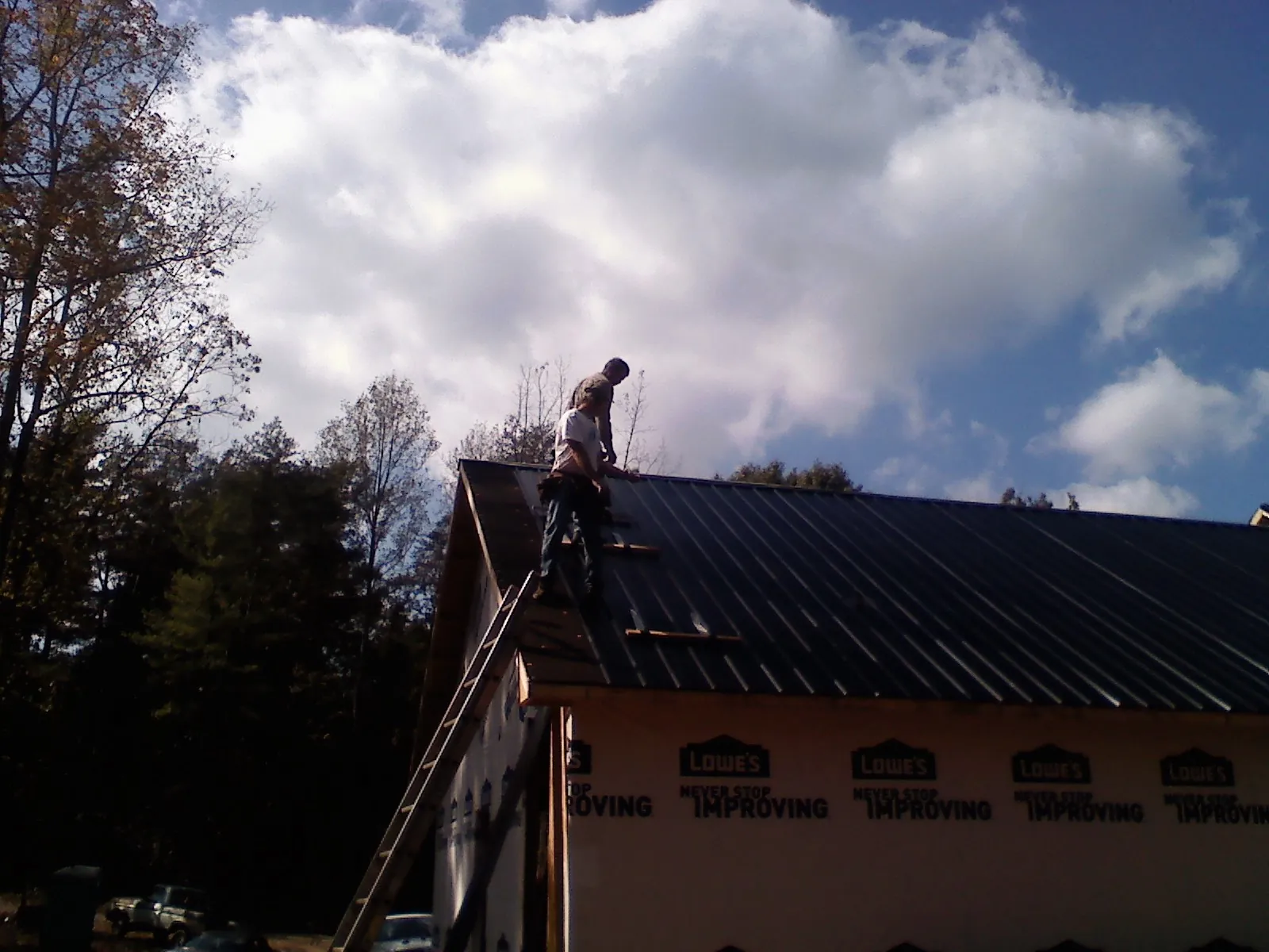 Roofer fastening dark metal panels high against a cloudy sky, from a Roof Inspection job in Weldona